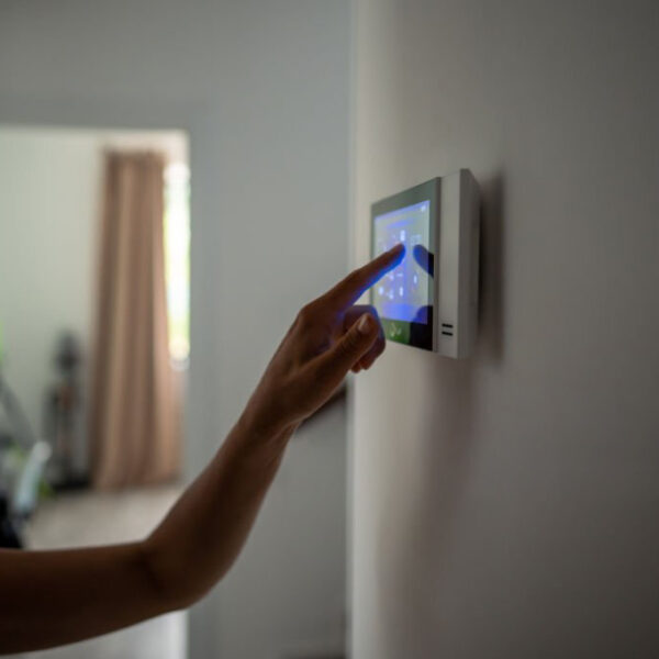 Closeup hand using smart home touch screen with connected appliances device on wall. Setting, checking energy security heating system on digital control in apartment. Home automation monitoring.